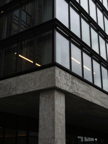 A sharp architectural close-up of a modern concrete foundation meeting a glass facade, low-key dramatic lighting with a single gold light trail reflecting on the glass.
