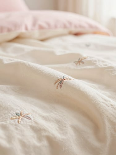 Close-up of soft cream fabric with delicate, minimal embroidery, hand-crafted details catching warm diffused sunlight, pastel tones, shallow depth of field
