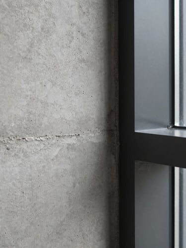 Close-up vertical shot of raw concrete texture meeting a matte black steel frame, sharp natural window light, minimalist architectural detail, 35mm