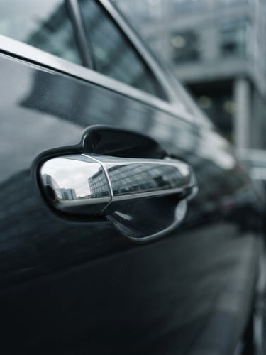 Close-up of a pristine executive sedan door handle, polished chrome reflecting cool overcast corporate architecture, shallow depth of field, 35mm