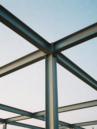 Low-angle heroic shot of structural steel framing against a crisp morning sky, cool steel and slate tones, architectural film photography, sharp focus, 35mm lens.