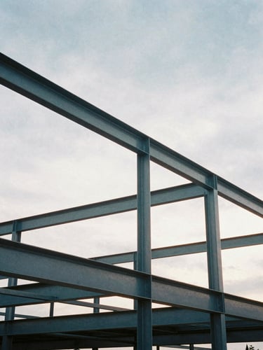 Low-angle architectural film photography of raw structural steel framing against a dramatic overcast morning sky, cool steel and slate tones, sharp focus, 35mm lens.