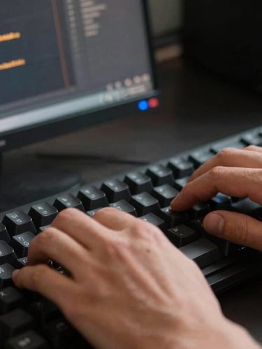 Close-up of developer hands typing on a mechanical keyboard, terminal screen reflecting amber code in a dark workspace.