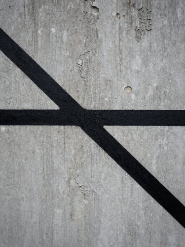 Extreme close-up of a sharp, stark black painted line cutting across a crumbling, textured grey concrete wall under overcast daylight.