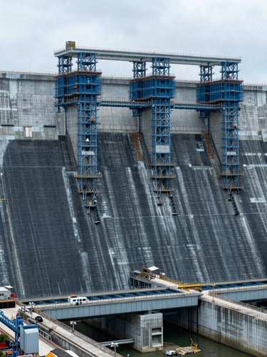 Wide panoramic view of a massive hydroelectric dam under construction in Malaysia, cool overcast daylight, sharp technical detail, structural steel blue tones