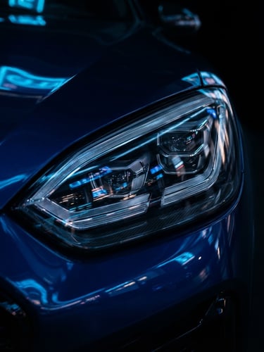 Sleek modern luxury electric vehicle headlight reflecting neon blue city lights, dark studio background, sharp focus, 85mm