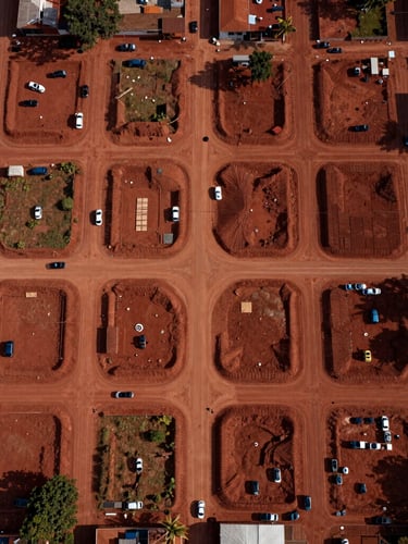 Top-down orthographic drone view of an emerging urban grid in Paraguay, clean dirt roads carved into red soil, high-contrast morning light emphasizing structural layout
