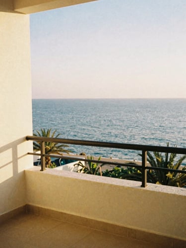 A quiet sun-drenched resort balcony overlooking the Mediterranean sea, warm golden hour light, soft coastal tones, 35mm film