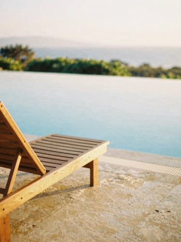 A sun-drenched quiet resort corner with a wooden lounge chair beside a calm turquoise pool, warm golden hour light, shallow depth of field, 35mm film
