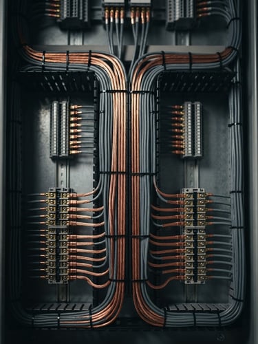 Symmetrical close-up of a meticulously dressed electrical panel with copper and slate wires run in perfect parallel lines, dramatic directional lighting