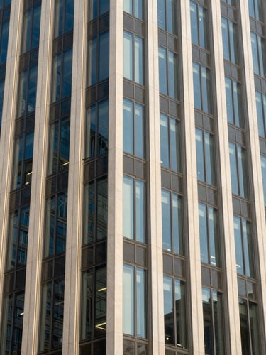 Crisp architectural photography of a modern financial center facade, sharp geometric patterns, bright daylight with cool blue and warm champagne highlights, 35mm lens.