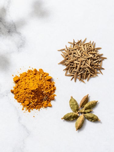 Bright overhead flat-lay of turmeric, cumin, and cardamom on a clean white marble background with soft natural daylight.