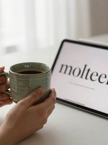 Warm editorial photography of hands holding a handmade ceramic coffee mug next to an open tablet screen showing clean serif typography. Soft morning window light, muted olive tones, shallow depth of field.