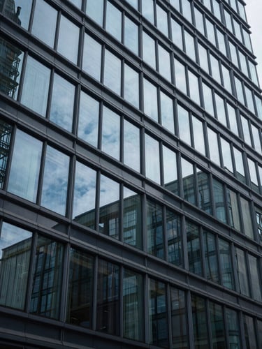 Wide architectural glass facade of a modern corporate headquarters, sharp geometric reflections, cool clinical lighting, deep blue shadows, high contrast.