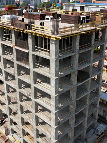Wide-angle overhead shot of an active multi-story tower construction site, concrete columns and steel rebar grids visible across multiple floors, clear daylight, industrial scale conveying large material volumes in place