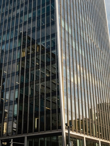 Sharp architectural crop of modern glass and steel skyscraper in London financial district, bright natural daylight, deep navy shadows, editorial style, 35mm lens