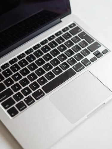 Overhead close-up of an open MacBook Pro on a clean white desk, keyboard in sharp focus, studio lighting from above, no people, precise and clinical framing