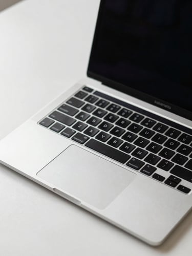 Close-up of a MacBook Pro open on a minimal white desk, keyboard and screen in sharp focus under neutral studio light, crisp clinical framing with no lifestyle elements, shot from slightly above at a three-quarter angle