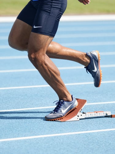 Dynamic close-up of a sprinter exploding out of blocks on a bright blue track, high-key natural daylight, crisp action freeze-frame, 35mm