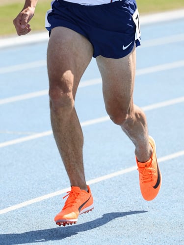 Bright high-key athletic photography, close-up of a focused athlete sprinting on a track in crisp natural daylight, vibrant orange details on shoes, sharp action freeze-frame, 35mm