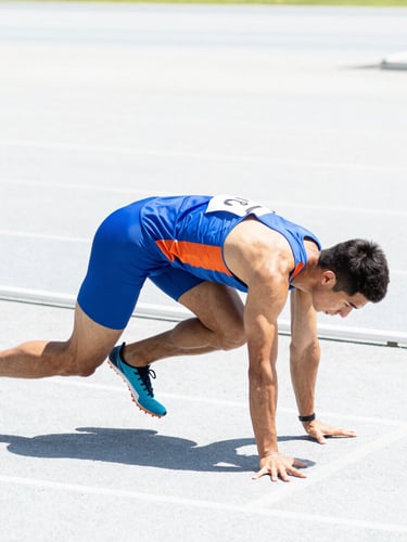 Bright high-key athletic photography, crisp natural daylight, a focused athlete preparing for a sprint on a clean track, dynamic side profile, sharp focus, 35mm