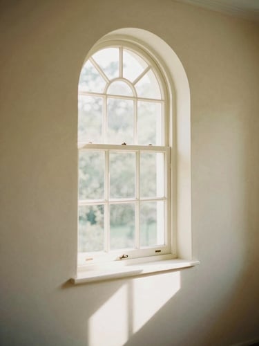Soft diffused daylight streaming through a clean arched window, casting long gentle shadows on a warm cream wall, peaceful atmosphere, 35mm photography