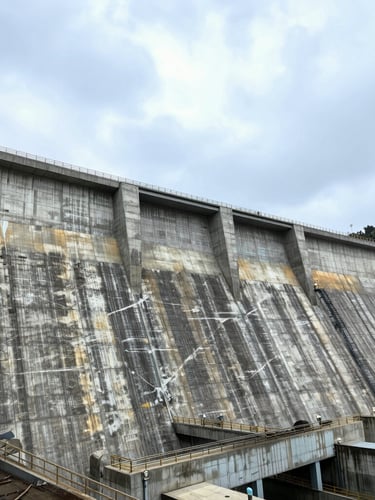 Dramatic wide-angle industrial photography of a massive concrete hydroelectric dam under a high-contrast overcast sky, 35mm lens.