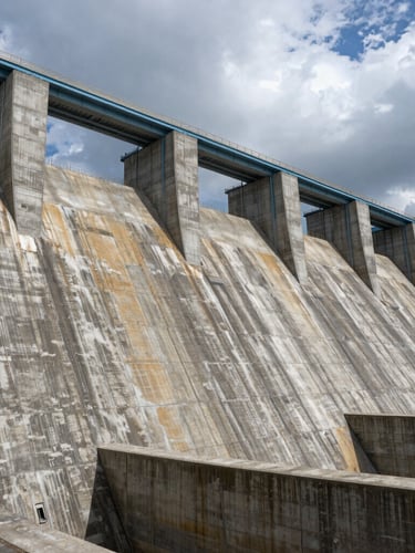 Extreme wide-angle dramatic industrial photography of a massive hydroelectric dam spillway, raw concrete textures under dramatic overcast daylight, steel blue tones, 35mm lens.