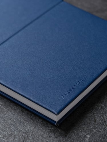 Macro close-up of a high-end physical brand book on a dark stone desk, crisp studio lighting, deep cobalt accents, sharp focus, Hasselblad medium format