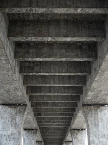 Looking straight up at the underside of a brutalist concrete overpass, repeating rectangular grid of beams converging to a vanishing point, sharp geometric lines, overcast even light, no people, purely formal composition