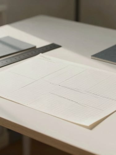 Architectural crop of a minimalist Layton design studio desk, showing technical grid paper, a metal ruler, and slate grey swatches under soft north-facing daylight.