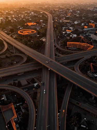 Aerial view of a complex highway interchange in India during golden hour, overlaid with a clean orange LiDAR point-cloud wireframe showing structural contours.