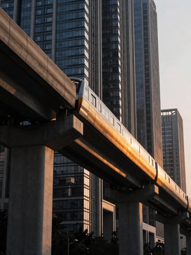 Dramatic low-angle architectural photograph of a high-speed metro rail viaduct slicing through a modern smart city skyline, golden hour lighting reflecting off concrete and steel, high-contrast matte black shadows.