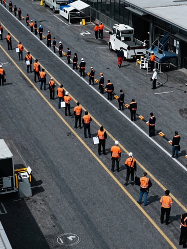 Primer plano de un plano técnico de seguridad y logística de eventos, con líneas de flujo de multitudes y puntos de control marcados en naranja de seguridad, bajo una iluminación fría y de alto contraste, con un enfoque nítido en el detalle, estilo documental arquitectónico.