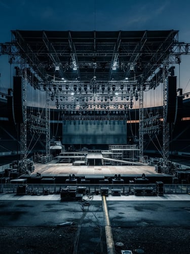Wide-angle shot of a massive, empty concert stage at twilight, intricate lighting rigs visible, focused on the main stage structure with a cool, high-contrast architectural documentary photography style.