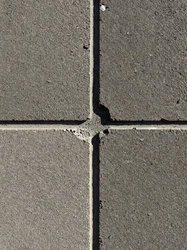 Close-up shot of troweled masonry joints under hard morning light, highlighting the gritty texture of concrete and stone