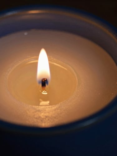 Macro editorial photograph of warm golden candle wax pooling inside a deep blue ceramic vessel, low-key candlelight, soft shadows, shallow depth of field.
