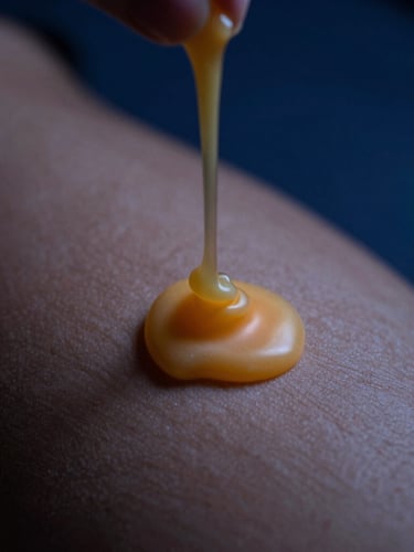 A slow, heavy pour of warm golden candle wax landing softly on bare skin, macro shot with shallow depth of field, low-key candlelight, deep cobalt blue shadows.