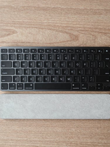 Top-down flat lay of a minimalist matte black aluminum keyboard and concrete wrist rest on a raw oak desk, soft diffused daylight, muted neutral tones, 50mm lens