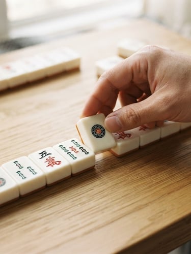 Macro close-up of minimalist white and vermillion mahjong tiles being arranged by hand on a light wooden table, soft natural daylight, 35mm
