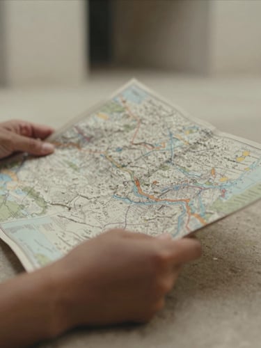 Close-up of tactile details, hands holding a textured heavy paper map on a stone surface, soft indirect daylight, muted tones, shallow depth of field.