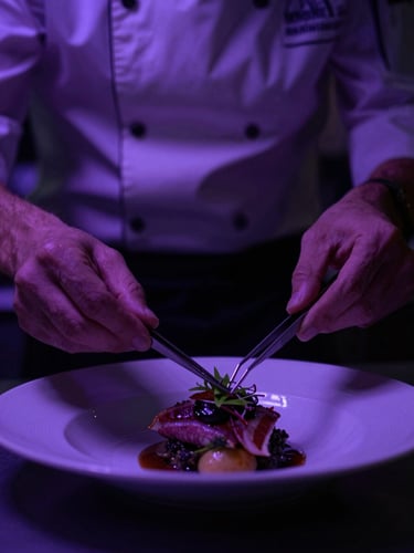 Dramatic close-up of a chef plating a dish with tweezers under moody violet kitchen lighting, high contrast, 35mm