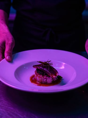 Dramatic close-up of a chef plating a dish under low-key violet and pink neon kitchen lighting, high contrast, 35mm