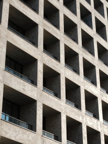 Crisp architectural detail of a modern concrete and steel high-rise facade under bright daylight, strong geometric lines and sharp shadows.