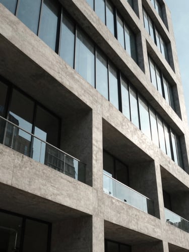 Wide architectural angle of a modern concrete and glass building facade, sharp geometric shadows, crisp daylight, high-contrast framing.