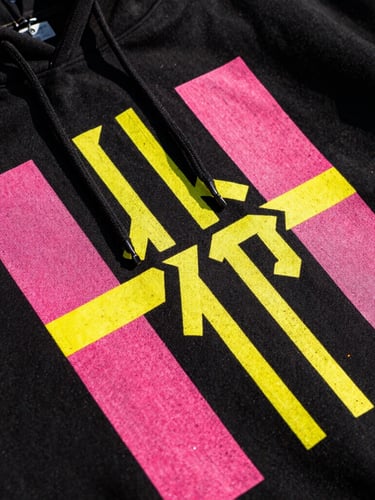 Extreme close-up of a high-contrast neon graphic print on a black streetwear hoodie, vibrant pink and yellow ink texture visible, flash photography