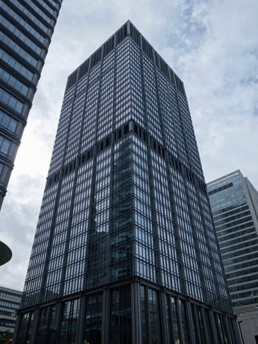 A sharp, wide-angle architectural shot of a modern financial center under cool, overcast daylight, with strong geometric shadows.