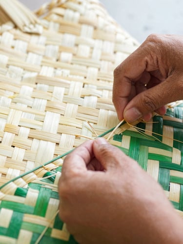 Close-up of Indonesian artisan's hands weaving natural fibers into a basket bag, focused on the intricate texture and motion, bright natural morning light, cheerful cream and green tones, detailed texture, 35mm