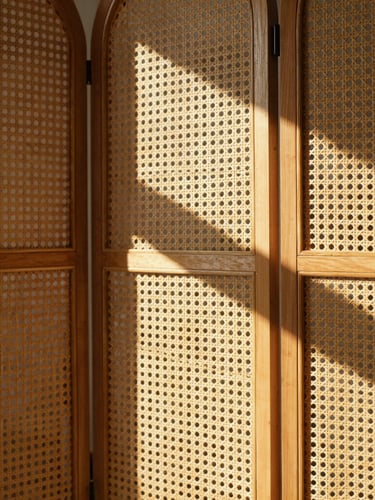Close-up of a folding woven rattan screen casting graphic geometric shadows in an airy room filled with warm afternoon light, architectural details