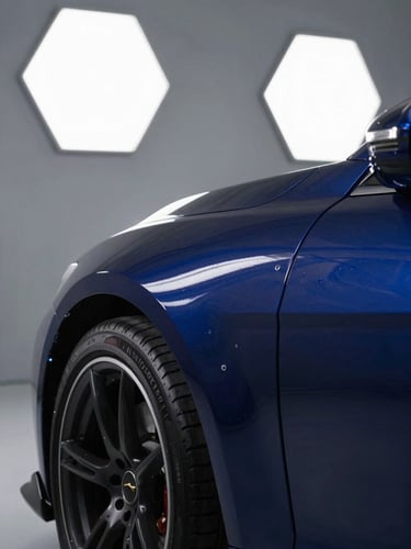 A close-up of a high-end sports car fender under bright LED hex-lights, showcasing deep metallic blue paint reflections and a crisp paint correction line, sharp focus, 35mm.